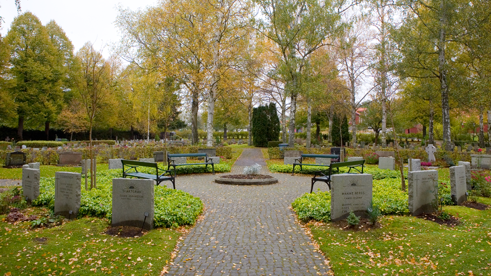 En kyrkogård där gravarna ligger i en cirkel runt en plats med bänkar och rabatter.
