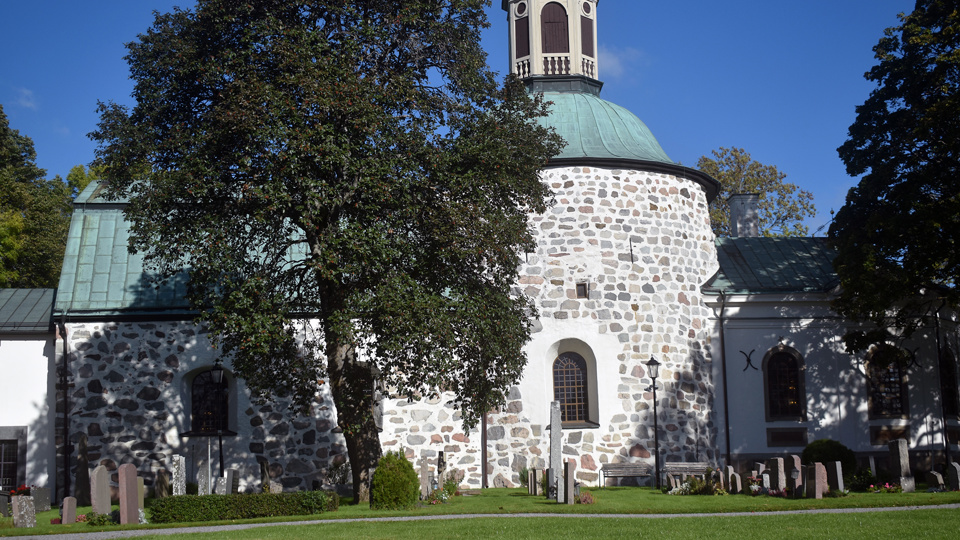 En vit stenkyrka med rundade väggar och träd på varje sida.