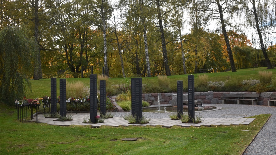 En askgravlund med en damm, gravmonument och blommande rabatter.