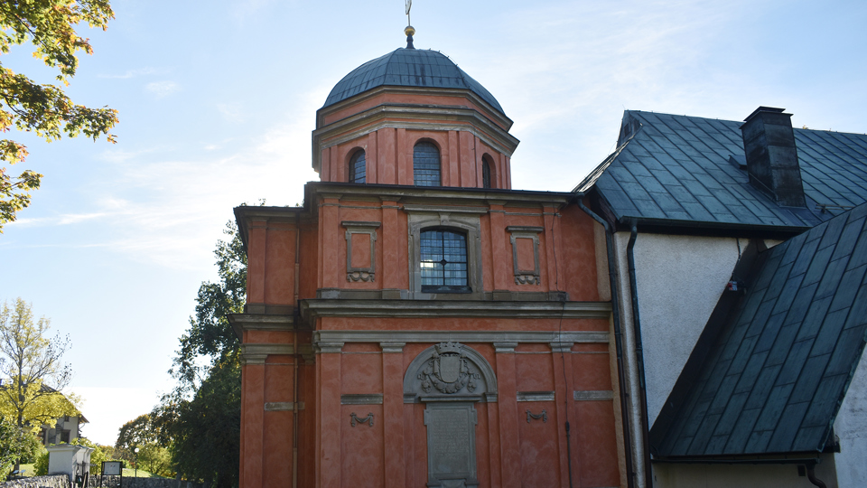 En tegelfärgad byggnad med åttakantigt torn som sitter i anslutning till en vit kyrka.