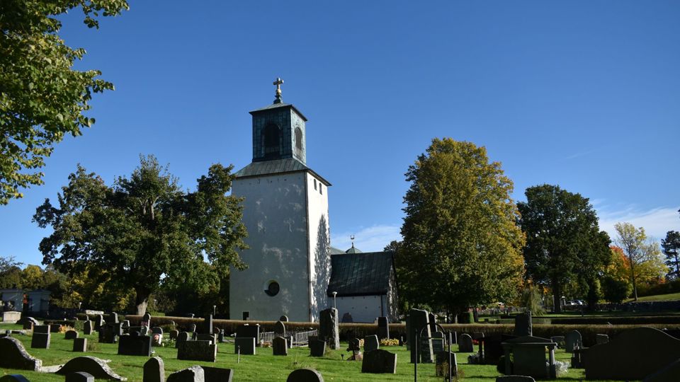 En vit kyrka omgiven av träd och en kyrkogård med gravstenar.