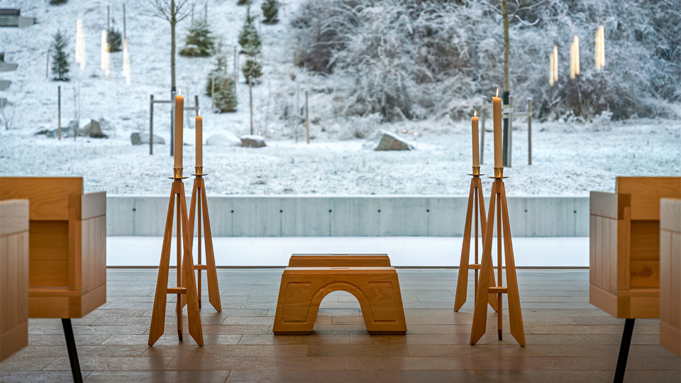 Två trähållare med ljus framför ett panoramafönster med vy över snöklädd omgivning.