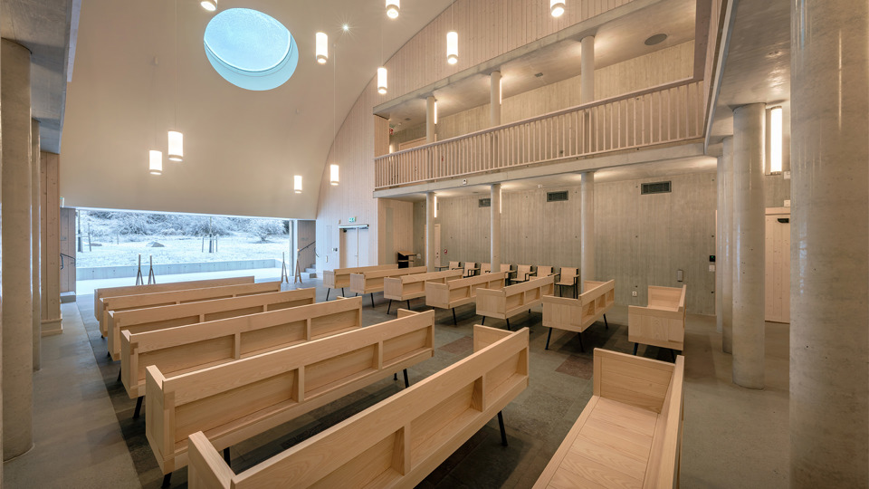 Vy uppifrån träläktaren ner till ceremonisalen med träbänkar och stort panoramafönster.