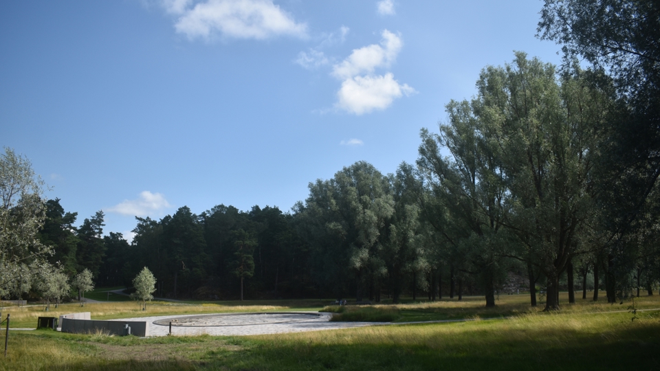 En rund stenlagd plats med bänkar på ett fält omgivet av skog.