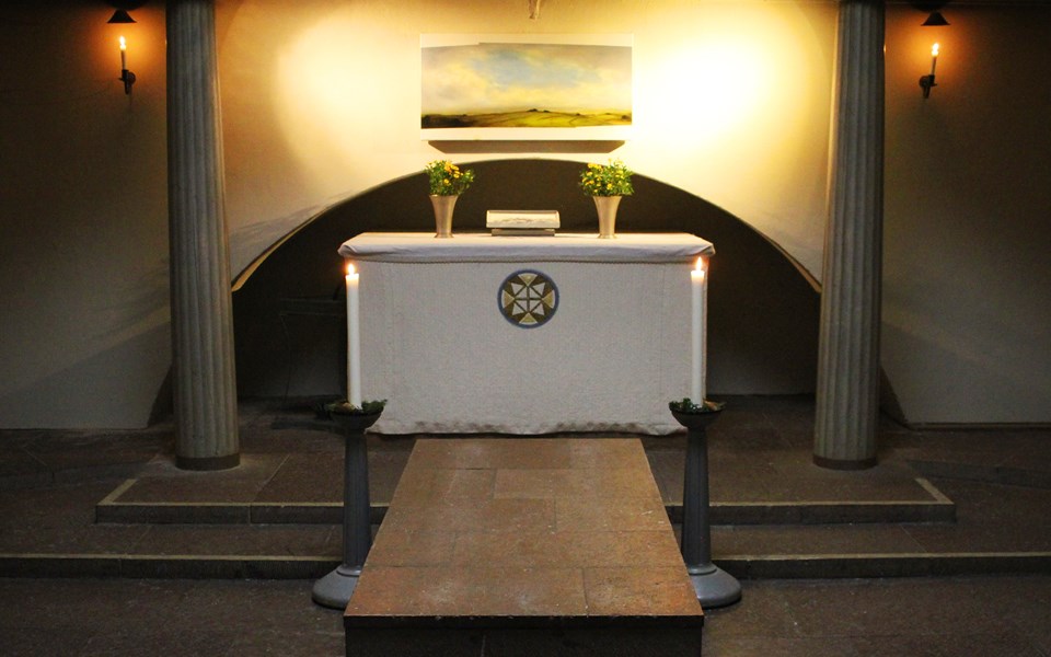 Stämningsfullt med tända ljus i kapell med altare och sten för kista.