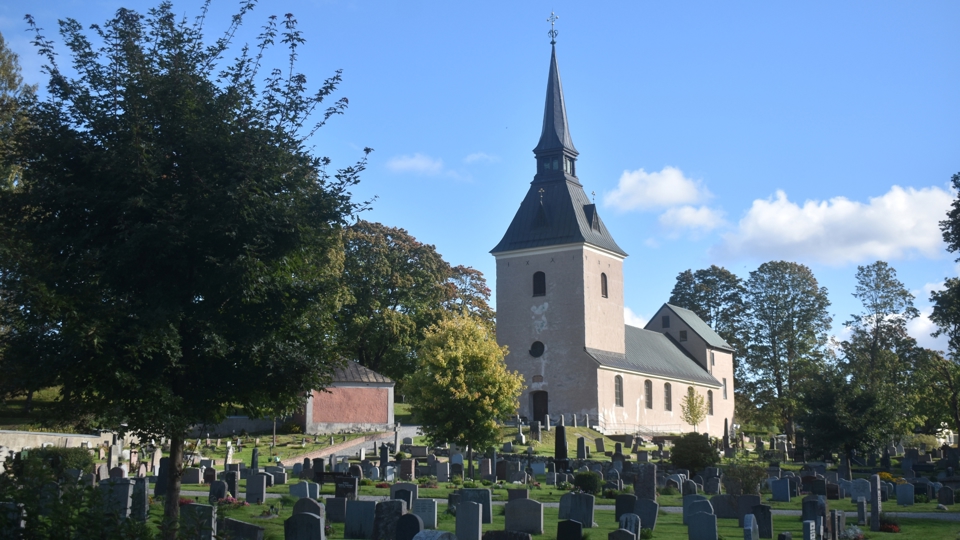 En begravningsplats med gravstenar och en kyrka i bakgrunden.
